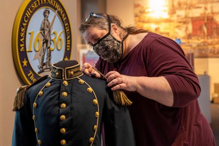 Person restoring historical military uniform in museum.
